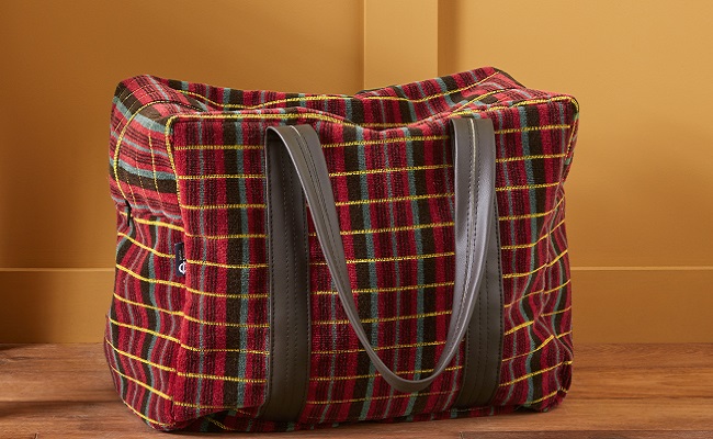 Routemaster moquette travel bag with two brown vita handles sitting against mustard yellow wall