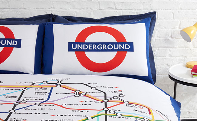 Colourful London Underground Map duvet cover on a bed with Underground roundel pillows propped up