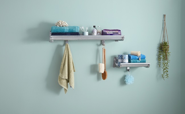 Two reproduction luggage racks, small and large, mounted on pale blue wall with towels folded on top